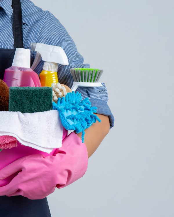Young girl is holding cleaning product, gloves and rags in the basin on white background